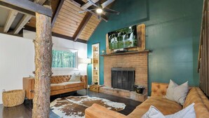 Ein gemütliches Wohnzimmer mit Kamin aus Backsteinen, einem großen Fernseher darüber und einem Ledersofa.