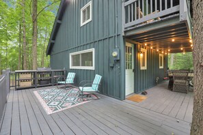 Relax on the deck with comfortable seating and a small table, surrounded by lush trees.