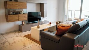 A modern living room with a flat-screen TV, a grey sofa, and a wooden cabinet with glass shelves. - Malta's Beachfront Apartment in Mellieha (Il-Mellieha)