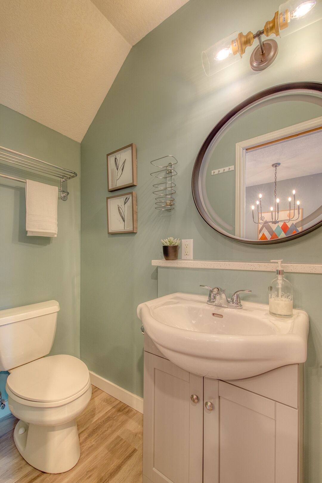 Un baño con inodoro blanco, lavabo con espejo y toallero.