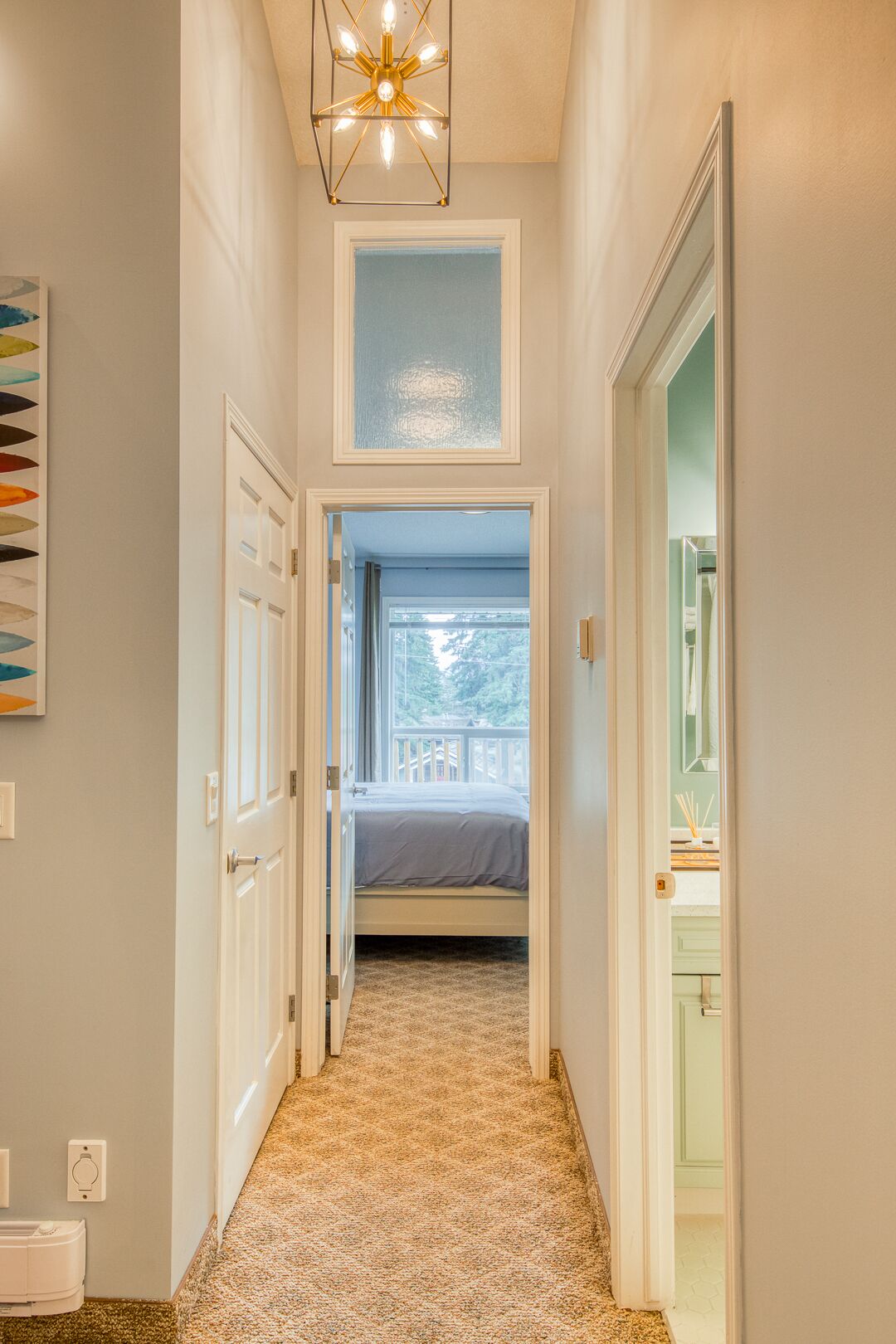 A hallway leading to a bedroom with a bed, a ceiling light fixture, and a view of the outdoors.