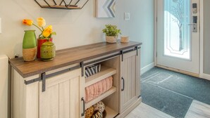 Um corredor com um console de madeira, uma prateleira de design geométrico e uma porta com painel de vidro jateado.