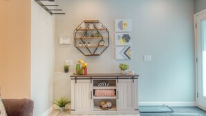 Uma sala de estar moderna com uma mesa de centro de madeira, um sofá, uma prateleira hexagonal na parede e uma porta com tapete.