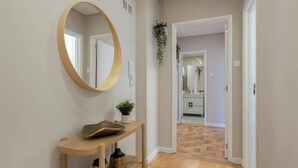 Ein Flur mit Holzboden, einem runden Spiegel, einem kleinen Tisch mit Pflanze und einer Tür zu einem Badezimmer.