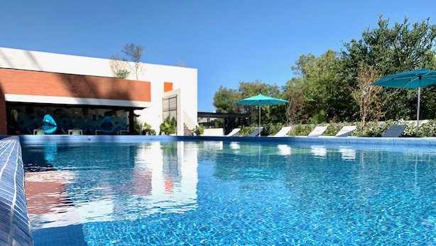 A clear swimming pool with lounge chairs and umbrellas, surrounded by greenery and a modern building. - Luxury & safety. PALCCO, Akron, ITESM, ValleReal (ZAPOPAN)