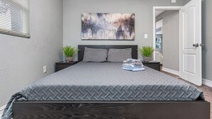 A bedroom with a large bed, a gray wall, a painting, and a door leading to another room.