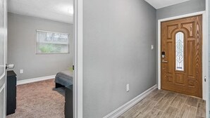A hallway with a wooden door, a window with blinds, and a carpeted area.