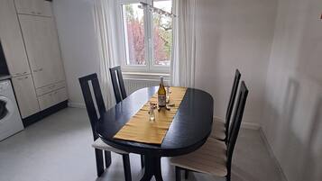 Ein Essbereich mit einem runden Tisch, schwarzen Stühlen, einer Weinflasche und einem Fenster mit Vorhängen.