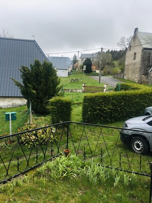 Un entorno rural con una carretera pavimentada, un coche aparcado y un edificio de piedra.
