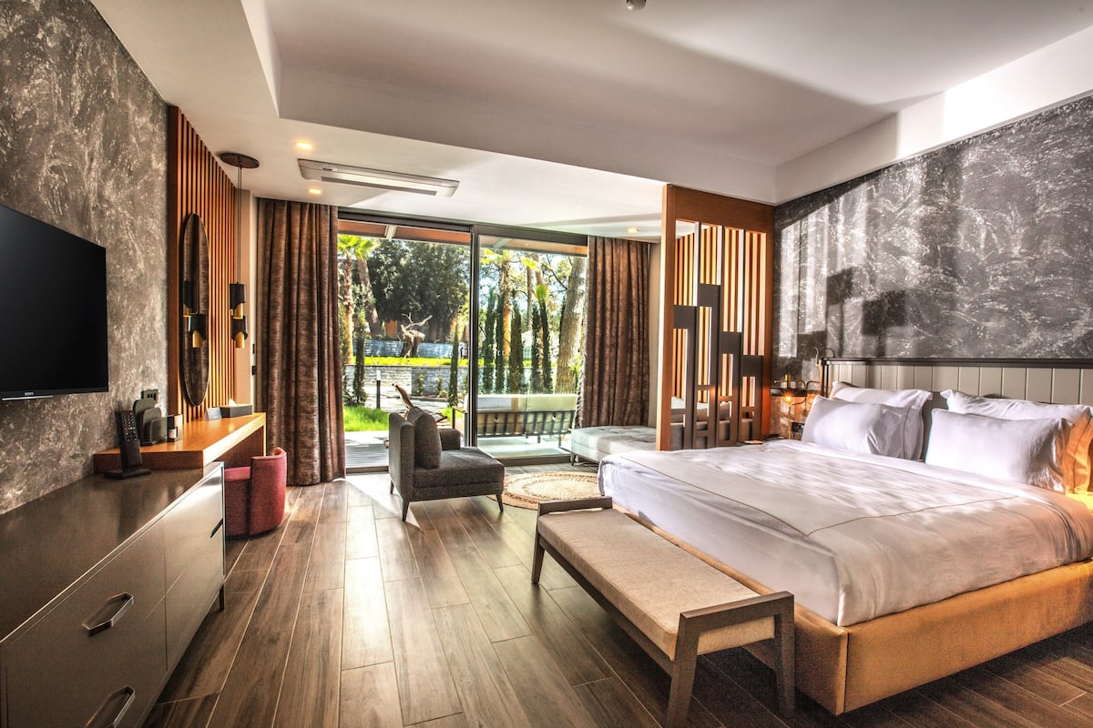 Quarto de hotel moderno com uma cama grande, uma TV, uma escrivaninha e vista para o exterior.