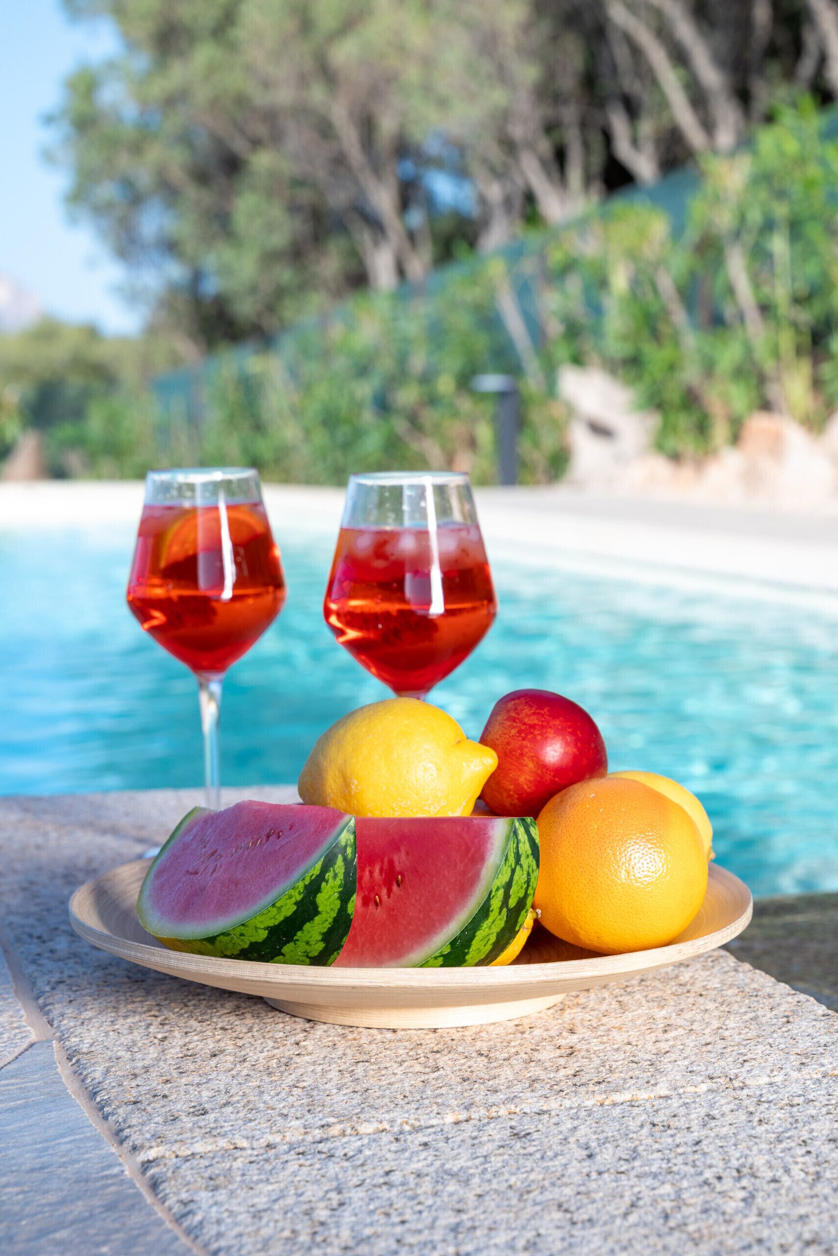 Ein Poolbereich mit einer Schüssel Wassermelone, Zitronen und Apfelscheiben sowie zwei Gläsern rotem Getränk.