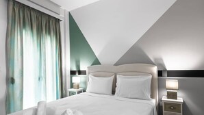 Ein modernes Hotelzimmer mit einem großen Bett, zwei Nachttischen mit Lampen und Blick ins Freie durch transparente Vorhänge.