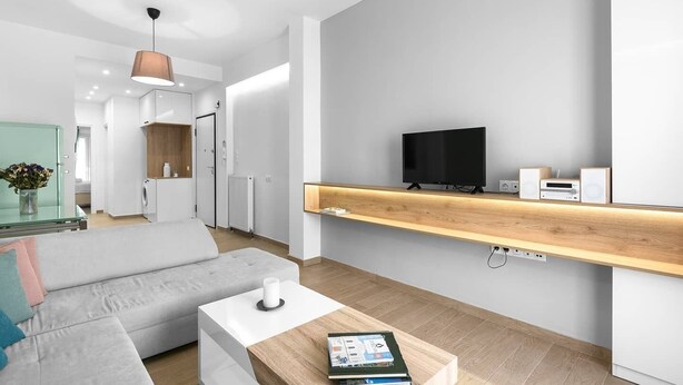 Ein modernes Wohnzimmer mit einer Couch, einem Couchtisch und einem Fernseher auf einem Holzregal.