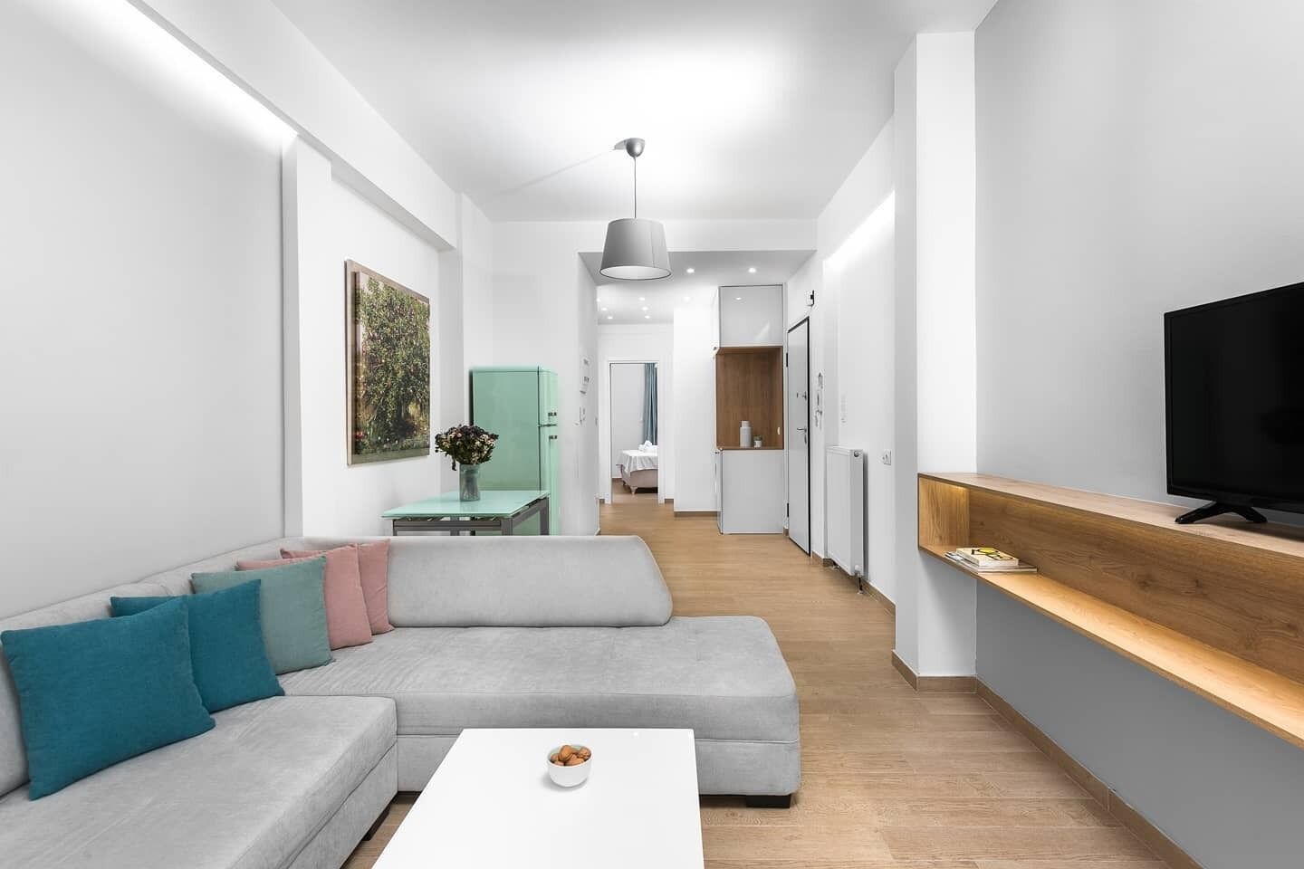 A modern living room with a grey sofa, a white coffee table, and a TV on a wooden shelf.
