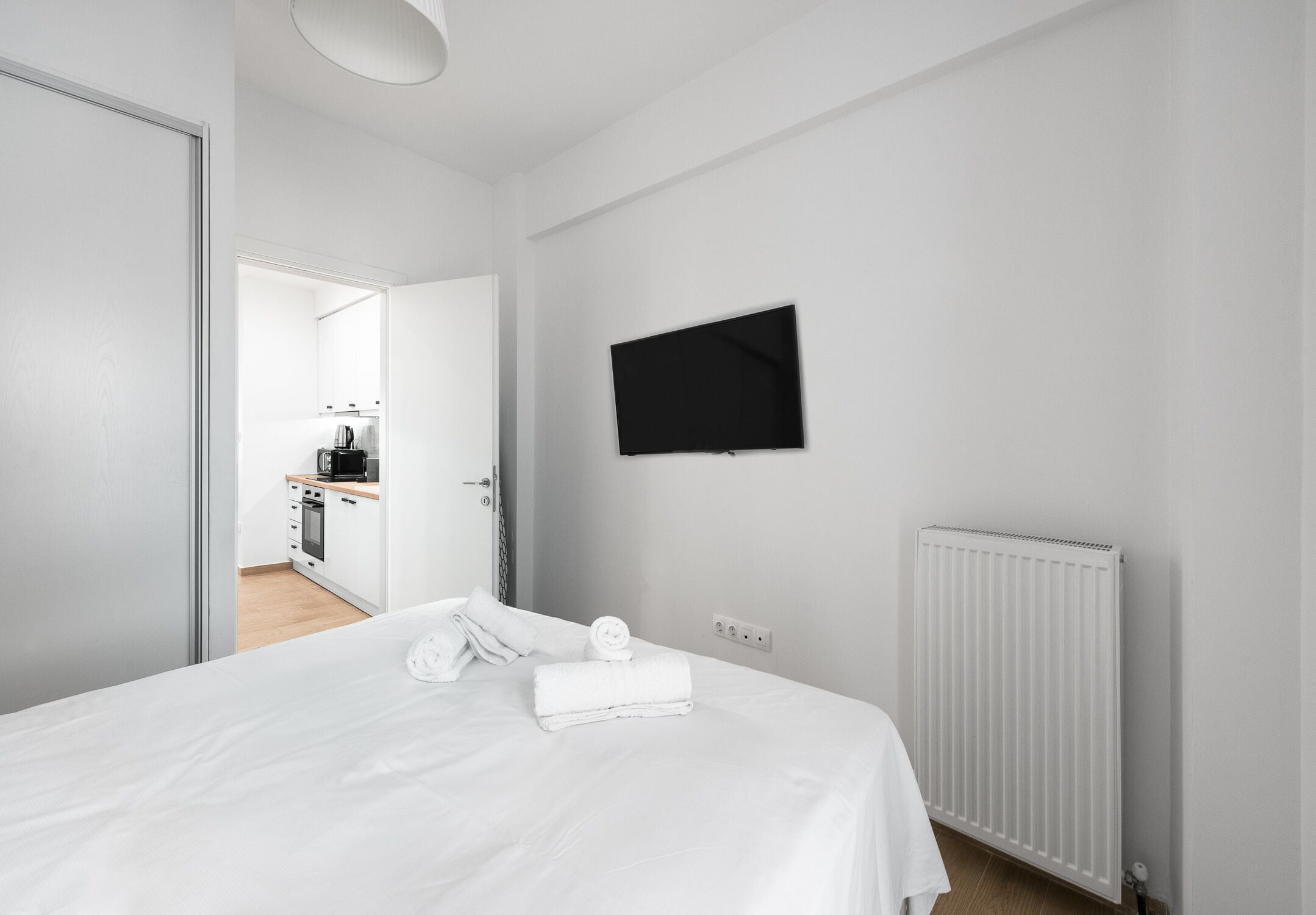 A modern hotel room with a bed, a flat-screen TV mounted on the wall, and a white radiator.
