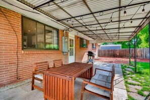 A covered patio with a wooden table and chairs, a grill, and a view of a backyard. - 5 Bedroom House with Crib - Walk to Downtown Littleton! (Littleton)