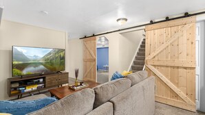 A living room with a large flat-screen TV, a wooden sliding door, a staircase, and a sofa.