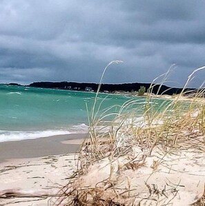 Une plage à l’eau turquoise et limpide, bordée d’un rivage sablonneux et de dunes herbeuses.