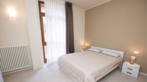 A bedroom with a bed, bedside lamps, a radiator, and a window with curtains. - Appartamenti l'Orologio - Le Lancette (Salò)