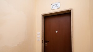 A closed wooden door with a sign above it that reads "Appartamento l'Orologio". There are three light switches on the wall to the left of the door. - Appartamenti l'Orologio - Le Lancette (Salò)