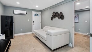 Una sala de estar moderna con un sofá blanco, un televisor de pantalla plana y un equipo de aire acondicionado en la pared.