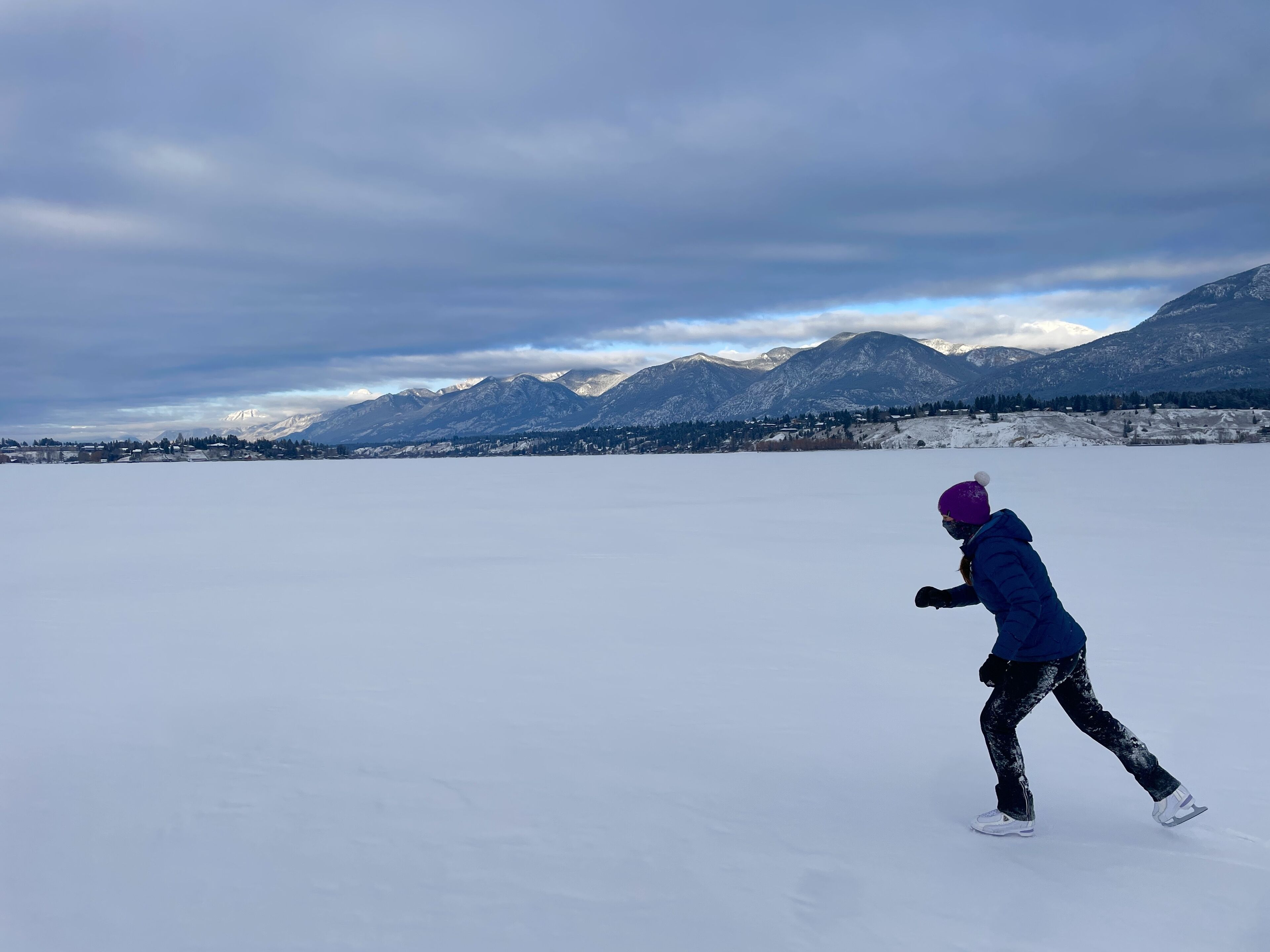 Une personne patine sur un lac gelé, avec des montagnes en arrière-plan.