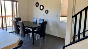 Un coin repas avec une table et des chaises, un escalier et une fenêtre avec des stores.