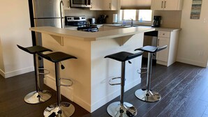 Une cuisine moderne dotée d’un îlot central, d’appareils électroménagers en acier inoxydable et de tabourets de bar.