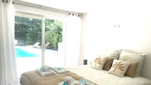 A bedroom with a large bed, a view of a swimming pool, and a sliding glass door.