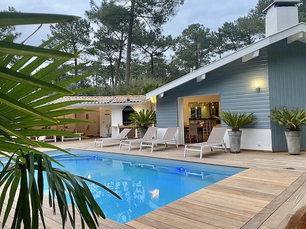 Un espace aménagé au bord de la piscine, avec des chaises longues, un barbecue et un coin repas.