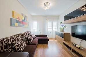 Een moderne woonkamer met een modulaire bank, een flatscreen televisie, houten vloeren en abstracte wanddecoratie.