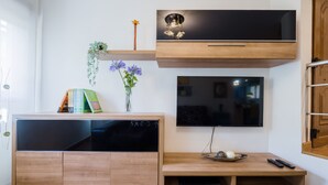 Ett modernt vardagsrum med ett träskåp, en platt-TV som är monterad på väggen och en liten hylla med dekorativa föremål.