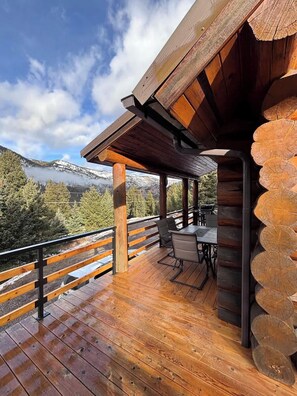 A wooden deck with a table and chairs, overlooking a mountainous landscape.