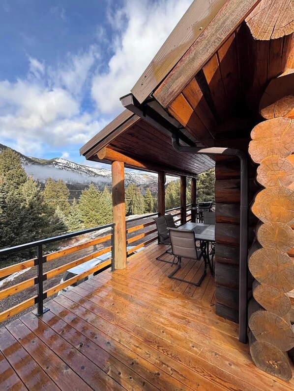 Une terrasse en bois avec une table et des chaises, offrant une vue sur un paysage montagneux.
