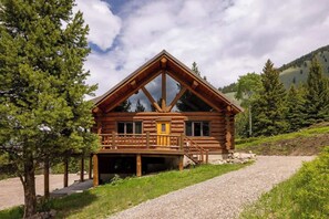 A log cabin with a balcony, a covered entrance, and a gravel driveway.