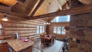 A log cabin interior with a dining area, kitchen, and stone fireplace.