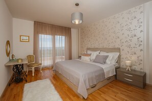 Ein Schlafzimmer mit einem großen Bett, einem Nachttisch, einem Sessel, einem Schreibtisch und einem Fenster mit Vorhängen.
