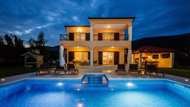 Casa de dos pisos con piscina frente a ella, con mobiliario exterior y un patio.