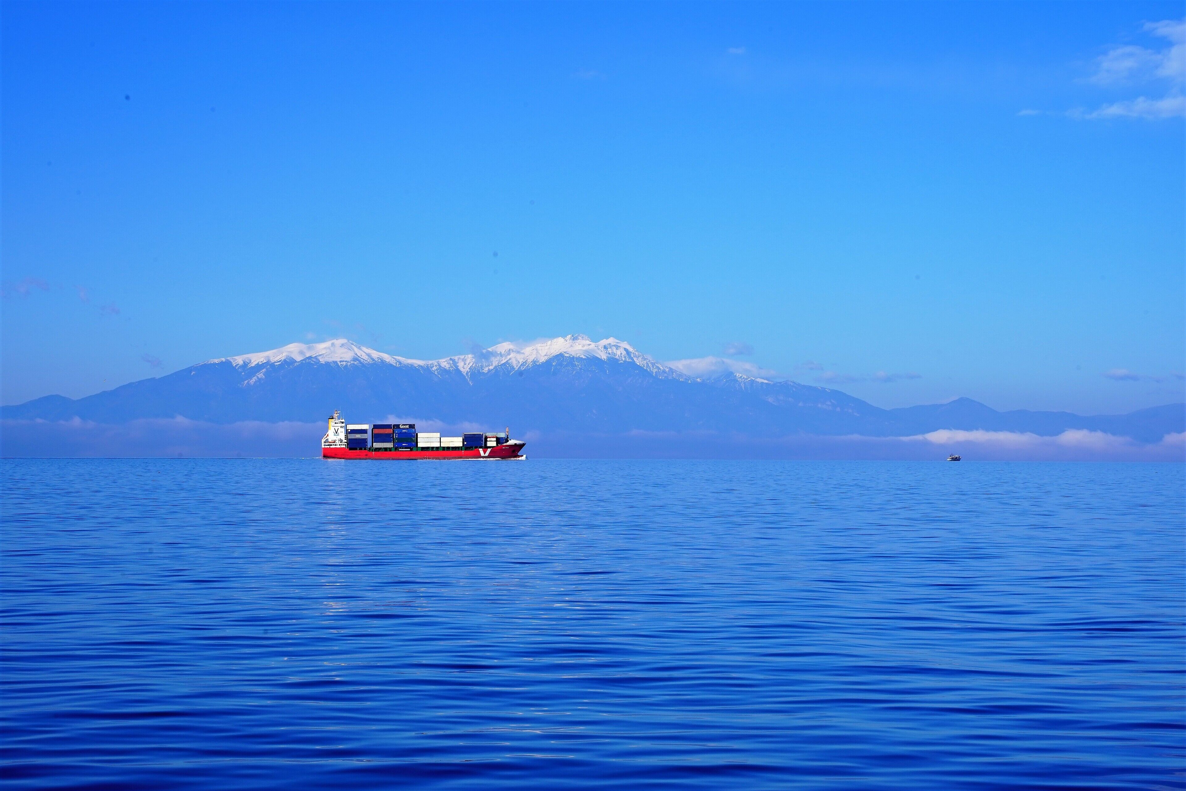 Een vrachtschip op kalm blauw water, met een berg met sneeuwkap op de achtergrond.