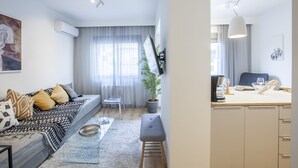 A modern living room with a sofa, a coffee table, and a dining area with a table and chairs. - Alterra Vita City Apartment (Thessaloniki)