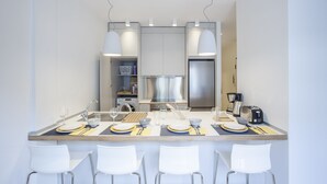 A modern kitchen with a central island, stainless steel appliances, and white chairs. - Alterra Vita City Apartment (Thessaloniki)