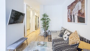 A modern living room with a sofa, bench, and a large painting on the wall. - Alterra Vita City Apartment (Thessaloniki)