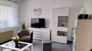 Un salon moderne avec un téléviseur à écran plat, un canapé, une table basse ornée de fleurs, un meuble et un radiateur.