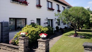 Un bâtiment blanc avec de nombreuses fenêtres et des jardinières remplies de fleurs. Un arbre se trouve dans le jardin.