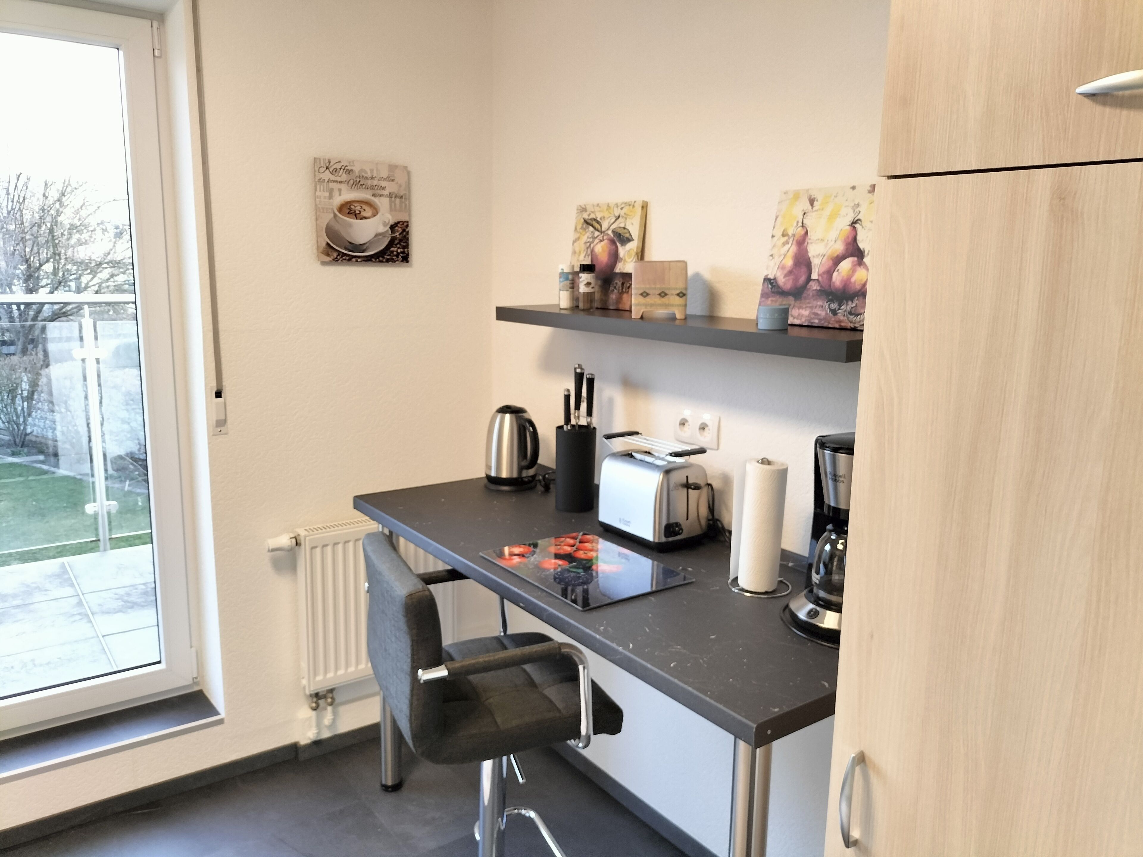 A compact kitchen with a window, a toaster, a kettle, and a chair.