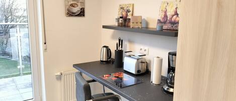 A compact kitchen with a window, a toaster, a kettle, and a chair.