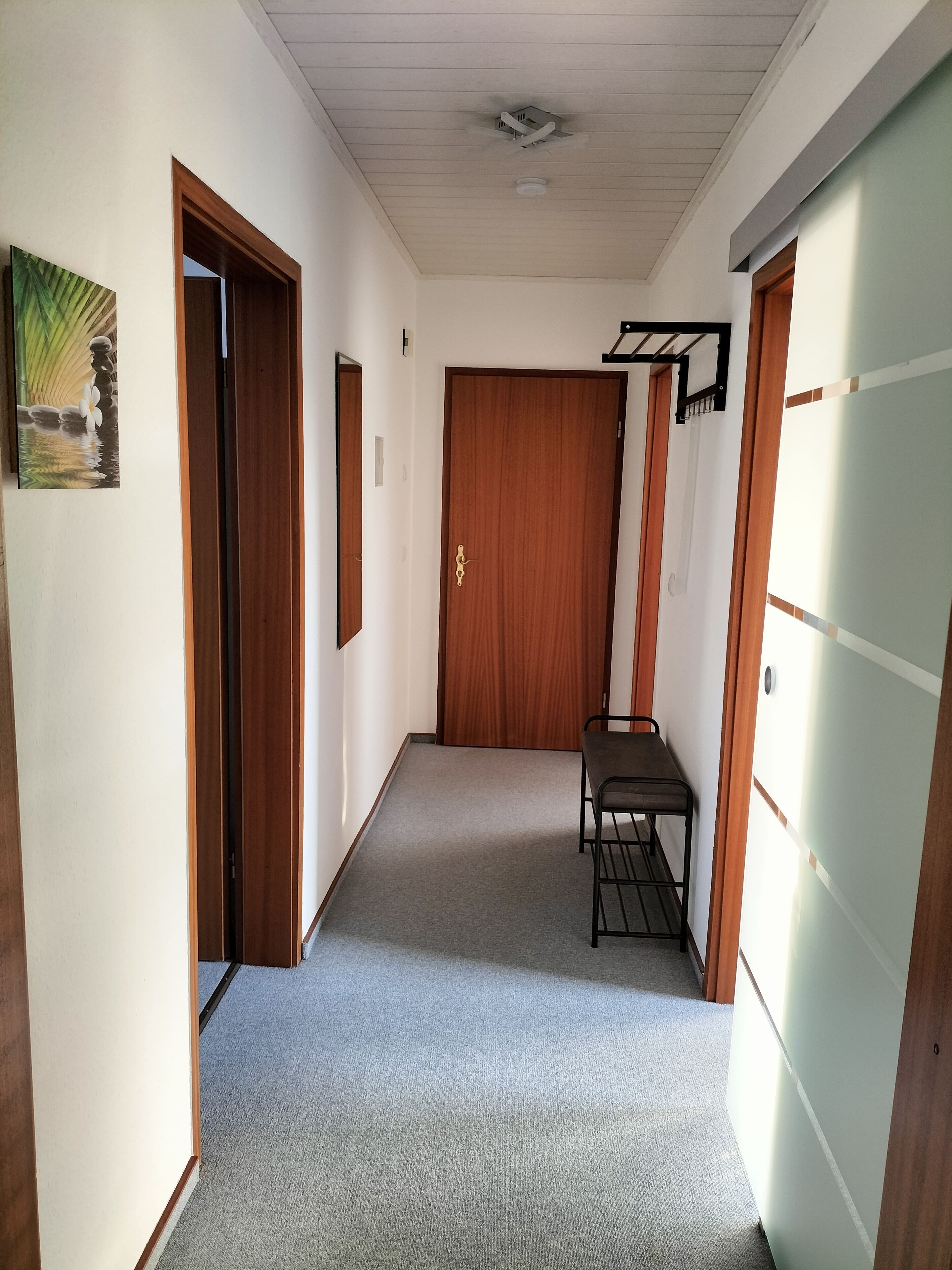 Un couloir doté d’un revêtement de sol en moquette, de portes en bois, d’une petite table avec des chaises et d’une bouche d’aération au plafond.