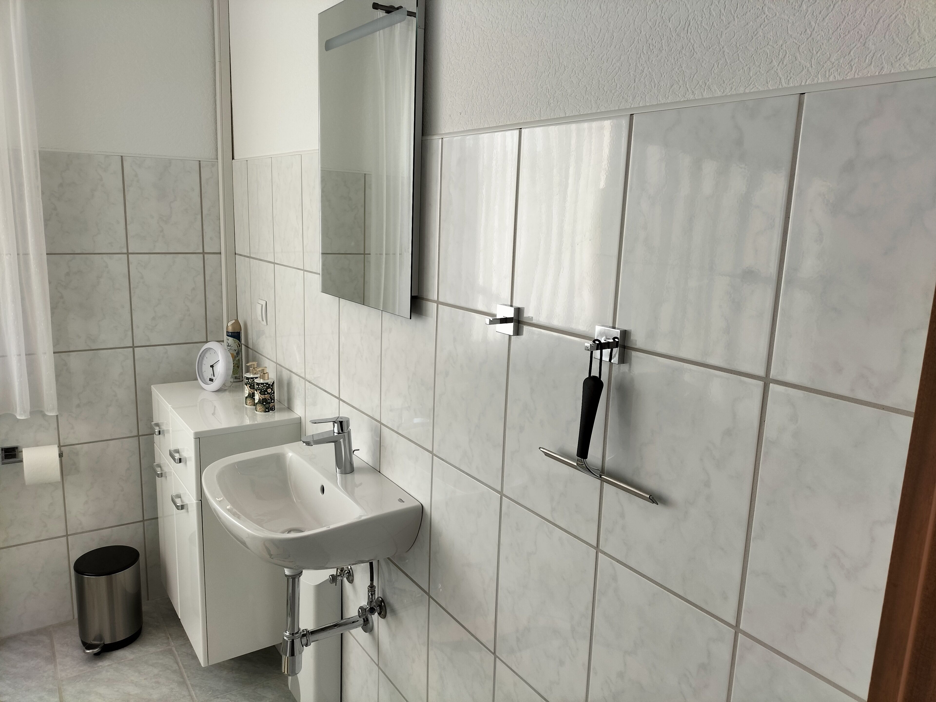 A modern bathroom with a white sink, mirror, and tiled walls.