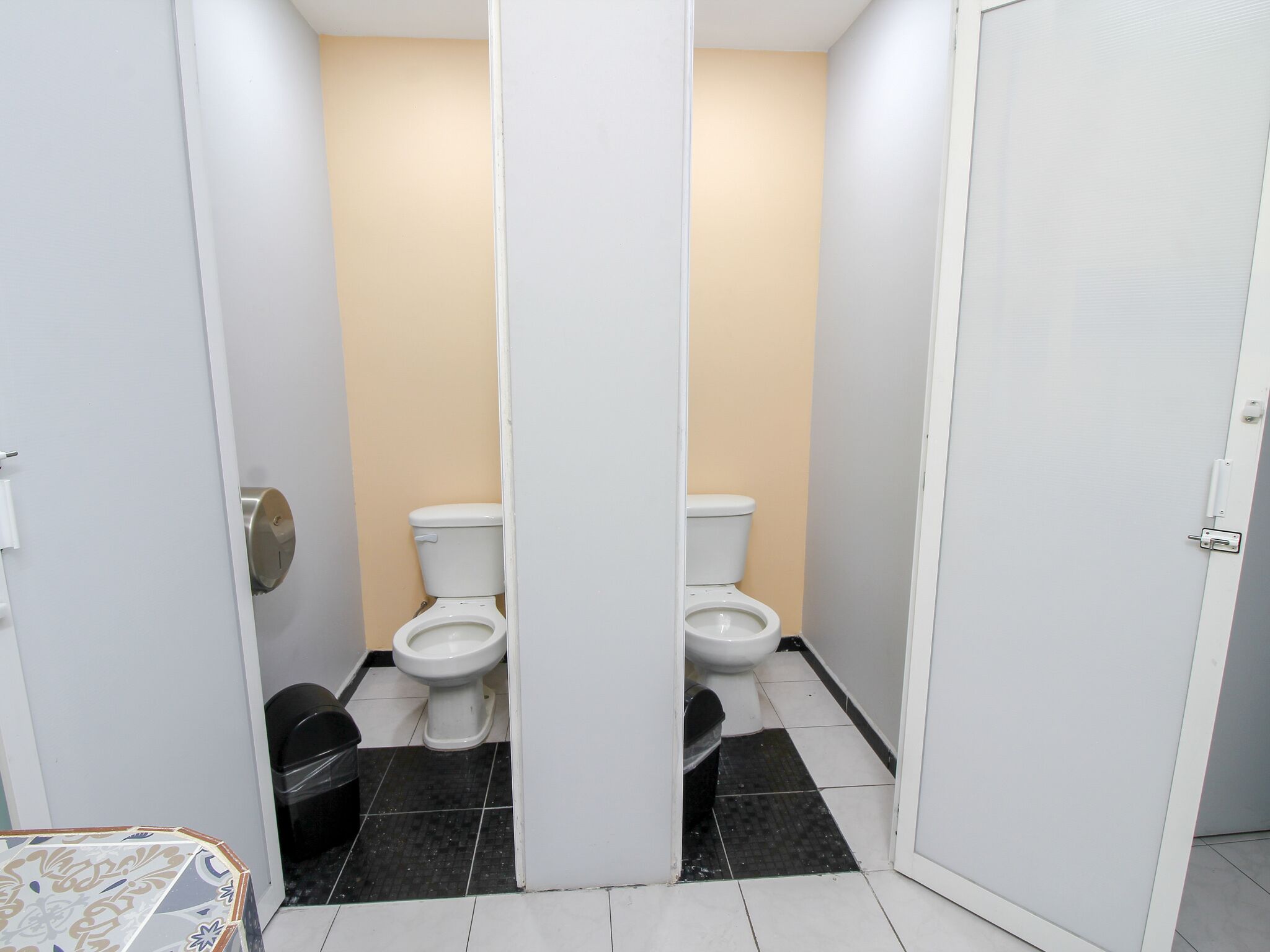 A small, narrow bathroom with two toilets, a trash bin, and a patterned table.