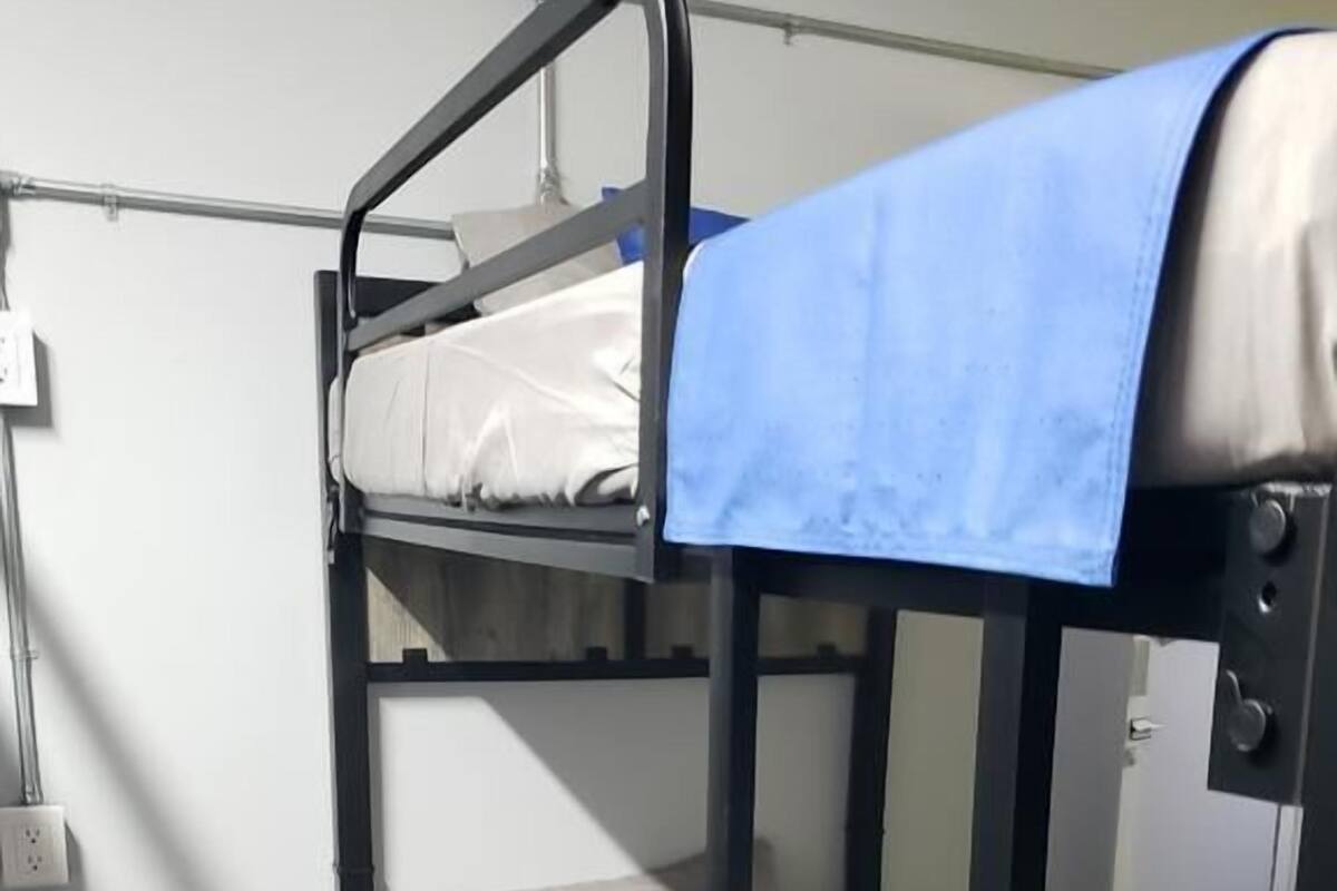 Een stapelbed met een blauwe deken en kussens, een witte muur en een deur op de achtergrond.